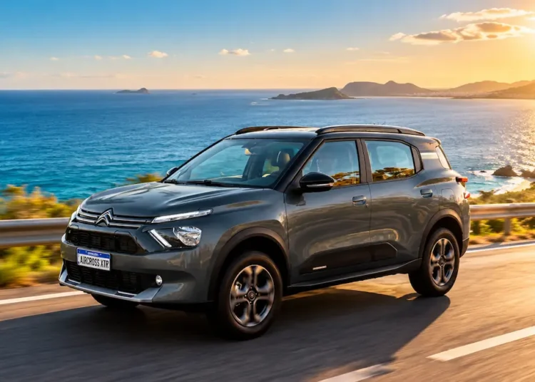 SUV cinza percorre uma estrada litorânea com o mar azul ao fundo, sob a luz intensa do sol.