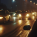 Trânsito intenso em avenida iluminada à noite com carros e faróis refletindo no asfalto molhado.