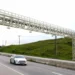 Pórtico de pedágio eletrônico Free Flow em rodovia com veículos passando pela estrutura de leitura automática.