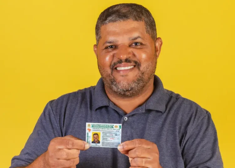 Homem segurando CNH e fundo amarelo.