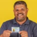 Homem segurando CNH e fundo amarelo.