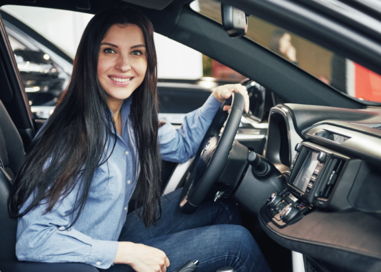 Mulher sorrindo ao volante de carro moderno em ambiente interno.