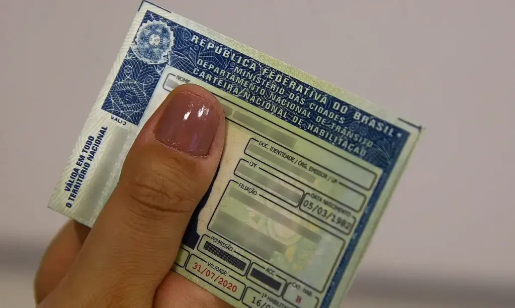 Mão segurando uma Carteira Nacional de Habilitação (CNH), ilustrando as regras de renovação automática para motoristas de 50 a 69 anos.