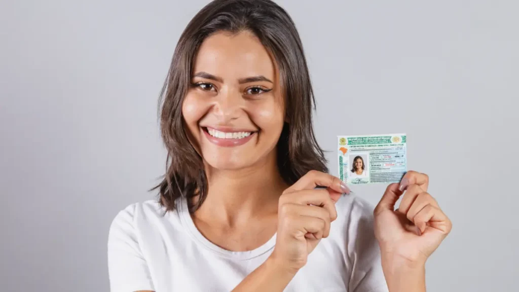 Jovem segurando CNH e fundo cinza.