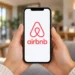 Mãos seguram um celular com o logotipo do Airbnb na tela.