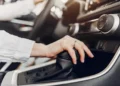 Mão sobre a alavanca de câmbio automático, com o console central do carro ao fundo.