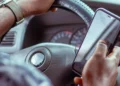 Mãos de um motorista segurando um celular junto ao volante do carro