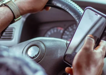 Mãos de um motorista segurando um celular junto ao volante do carro