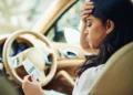 Mulher sentada ao volante, com a mão na testa, olhando um documento dentro do carro.