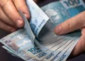 Mãos contando notas de R$ 100, representando a possibilidade de restituição de valores pagos indevidamente em multas de trânsito.