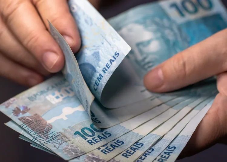 Mãos contando notas de R$ 100, representando a possibilidade de restituição de valores pagos indevidamente em multas de trânsito.