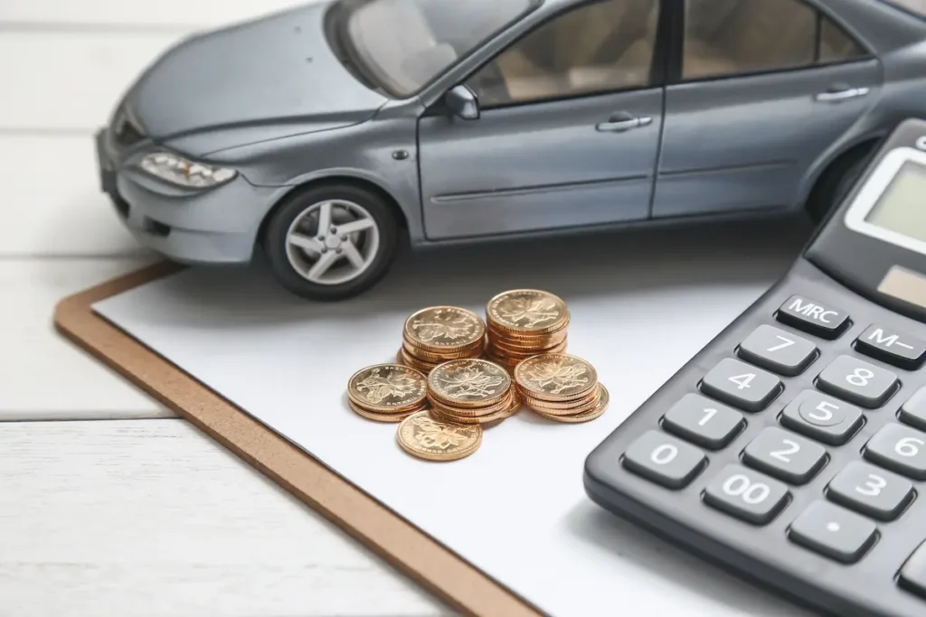 Miniatura de carro cinza ao lado de moedas e calculadora, representando o cálculo de valores para restituição de multas de trânsito.